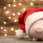 Piggy bank with Santa hat on table against blurred Christmas lights